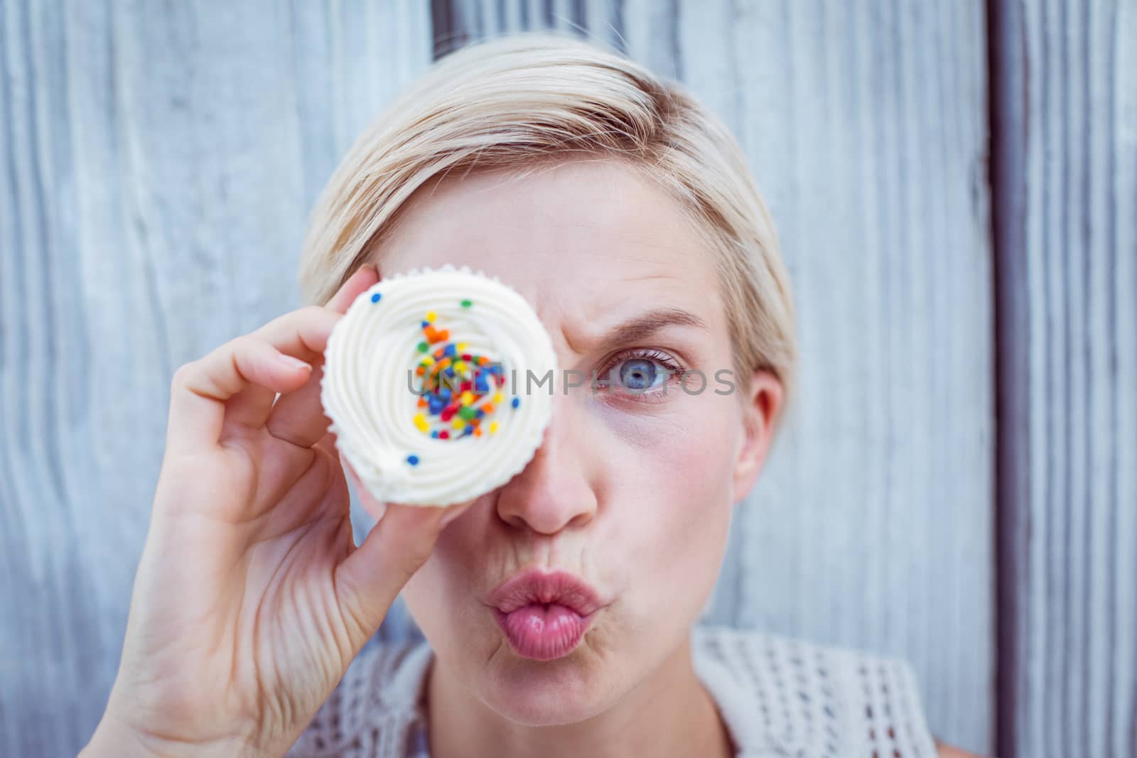 Pretty blonde woman grimacing with cupcake on wooden background