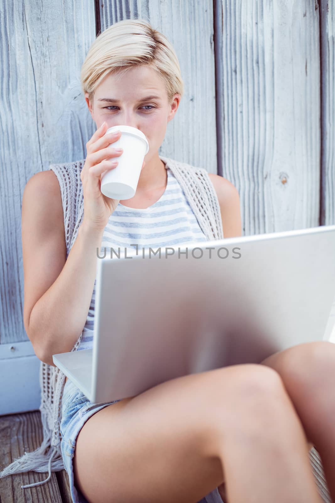Pretty blonde woman using her laptop and drinking coffee on wooden background