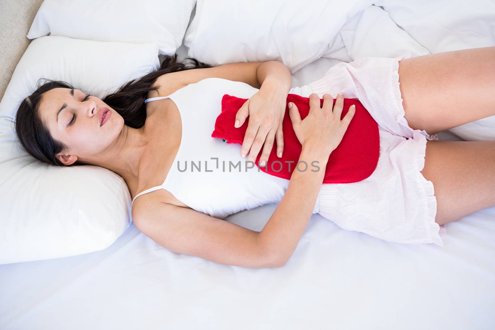 Pretty brunette with cramps on bed by Wavebreakmedia