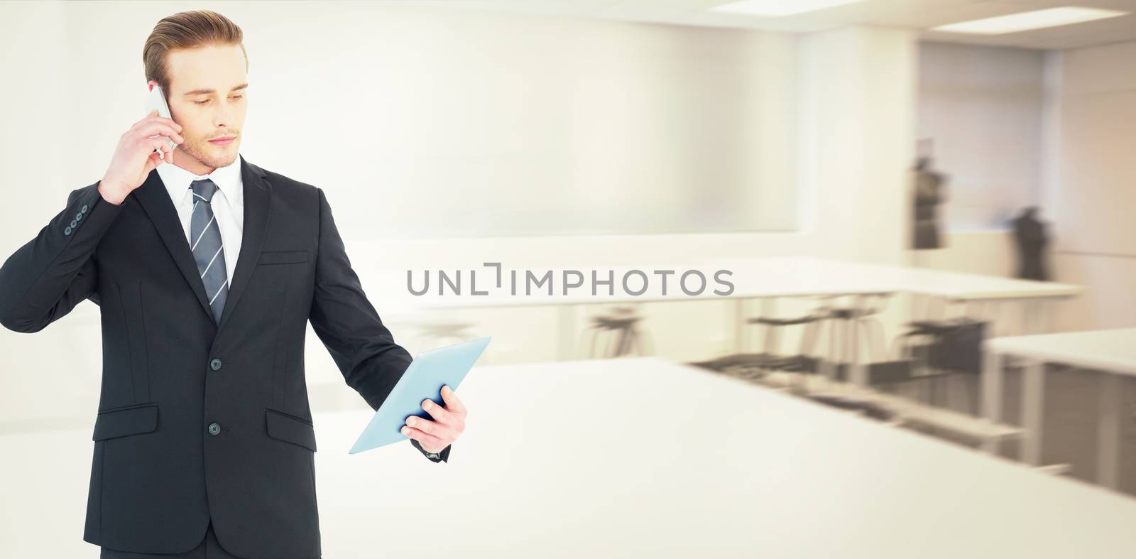 Serious businessman on the phone holding tablet against empty class room 