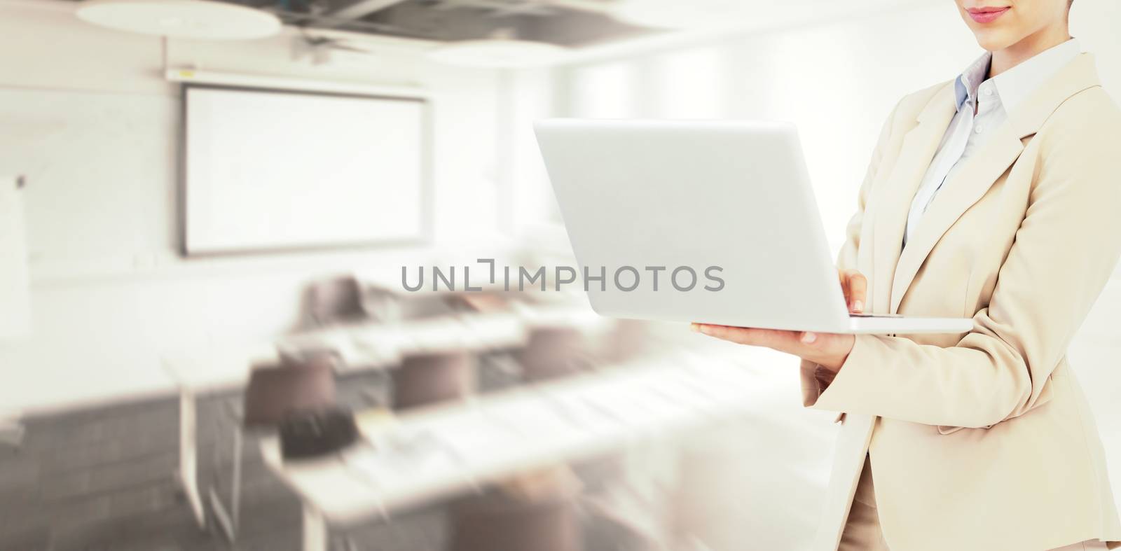 Confident businesswoman holding laptop against classroom