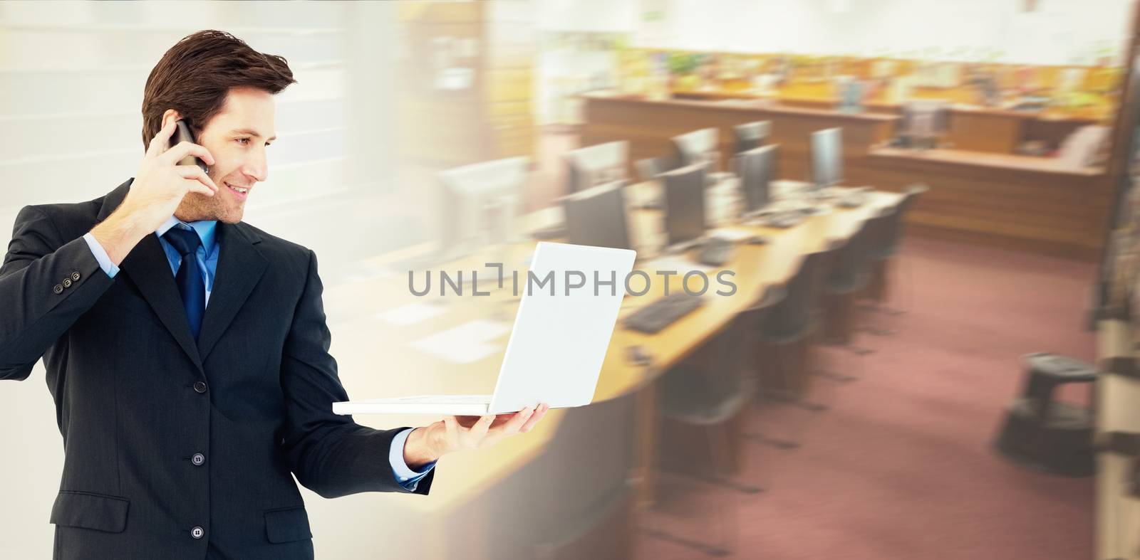 Businessman making a phone call while using a laptop against computer desks in the library