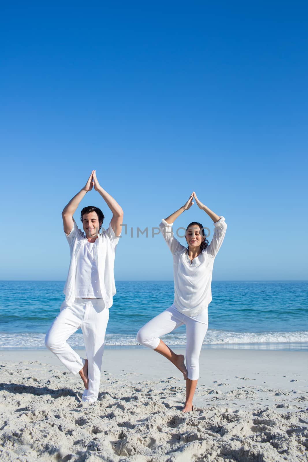 Happy couple doing yoga beside the water at the beach