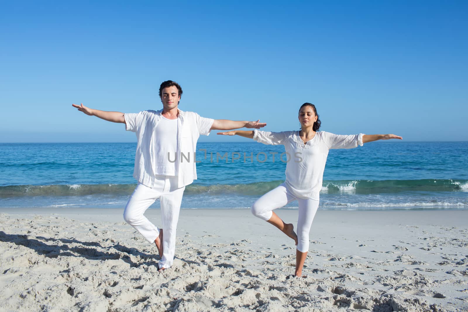Happy couple doing yoga beside the water at the beach