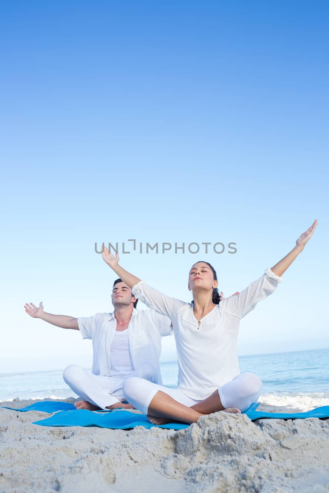 Happy couple doing yoga beside the water at the beach