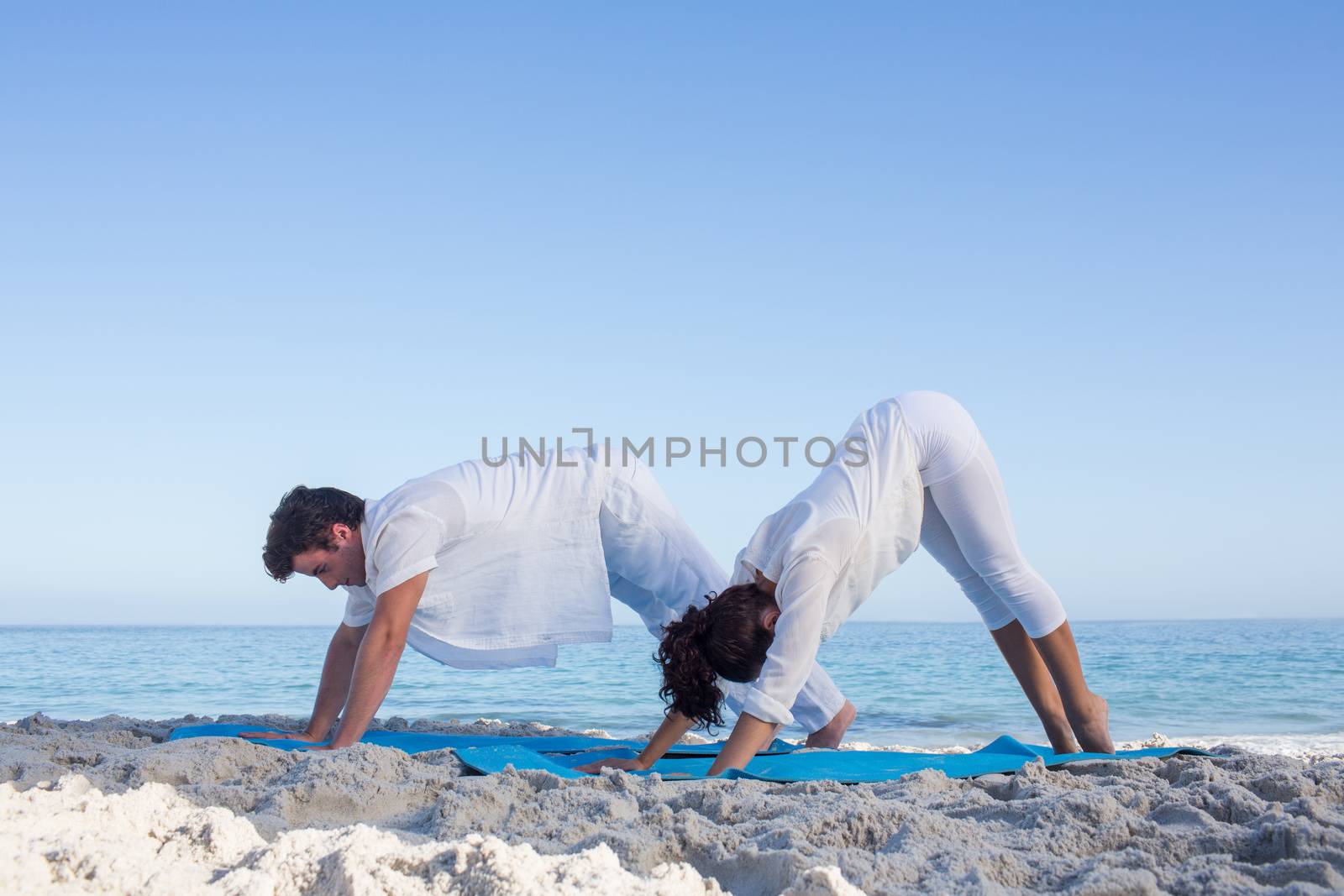 Happy couple doing yoga beside the water by Wavebreakmedia