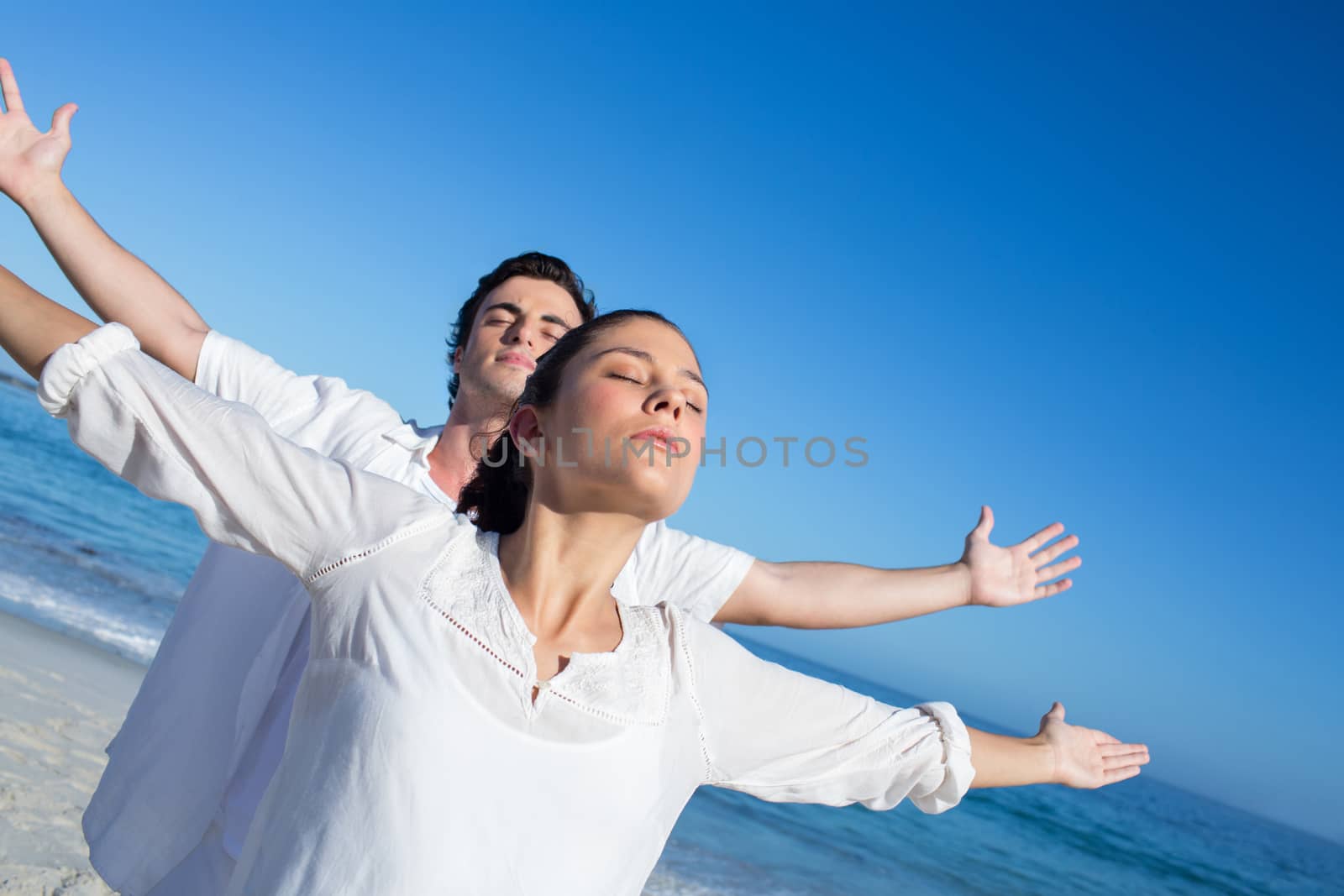 Happy couple doing yoga beside the water at the beach