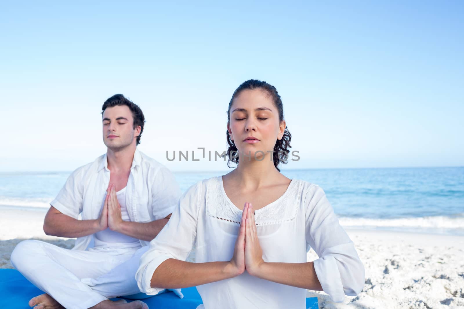 Happy couple doing yoga beside the water at the beach