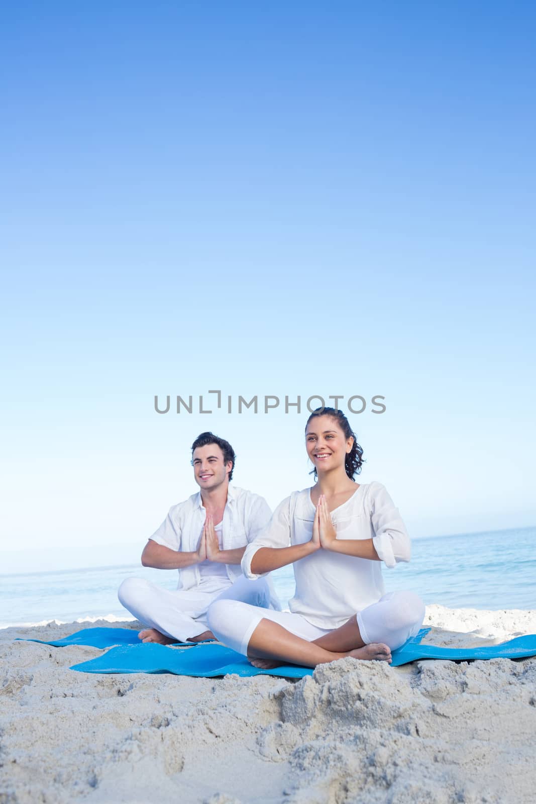 Happy couple doing yoga beside the water by Wavebreakmedia