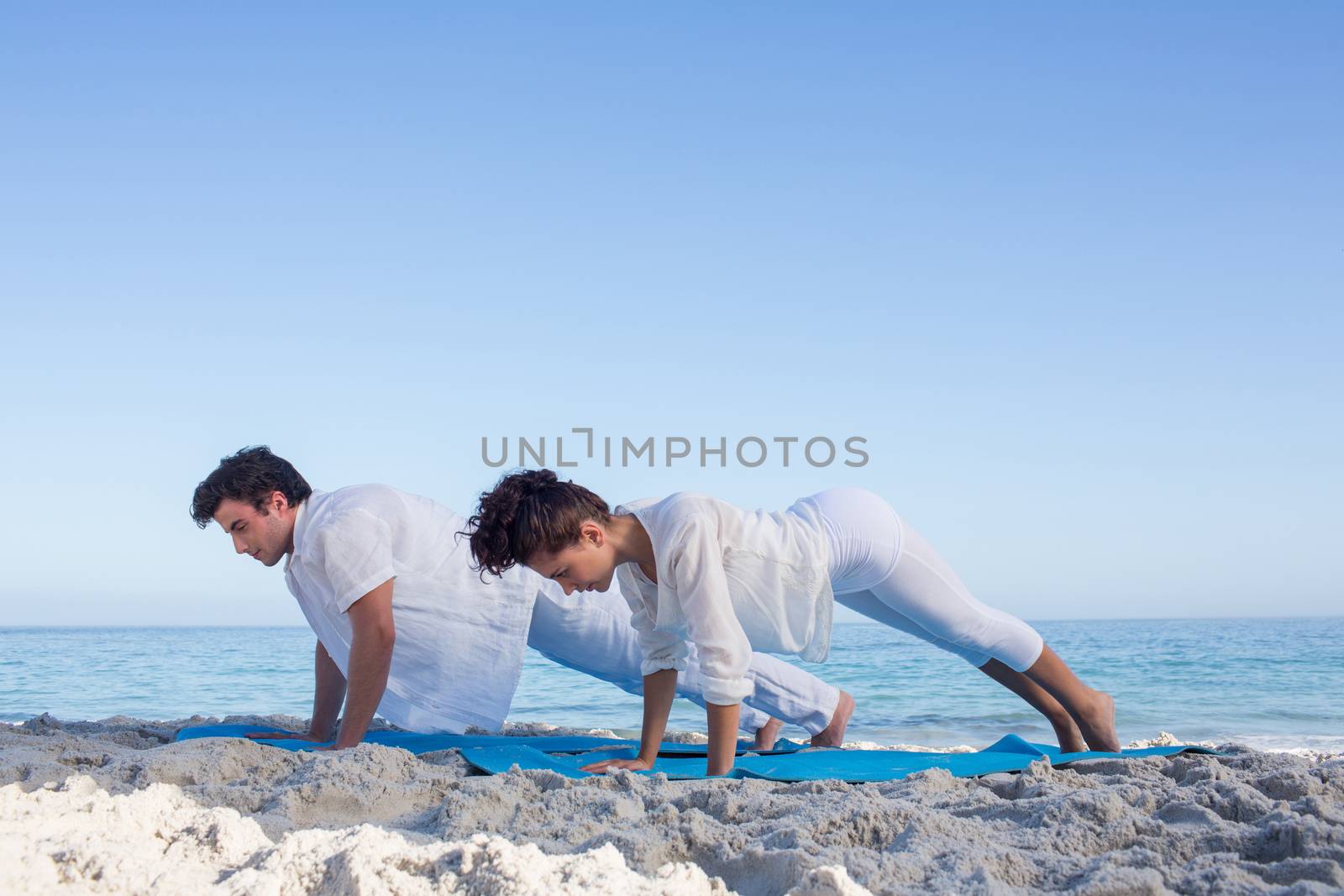 Happy couple doing yoga beside the water by Wavebreakmedia