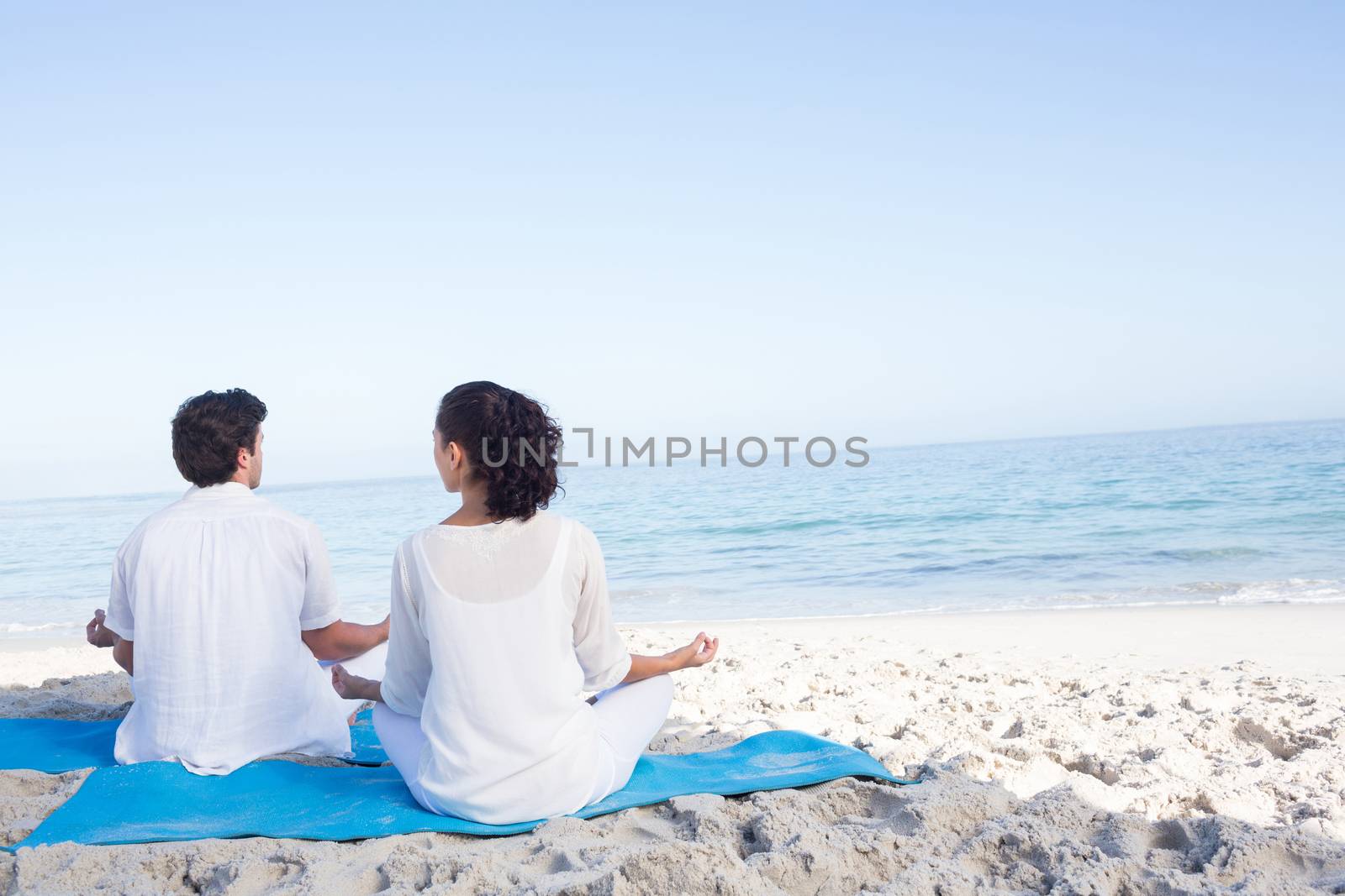 Happy couple doing yoga beside the water at the beach