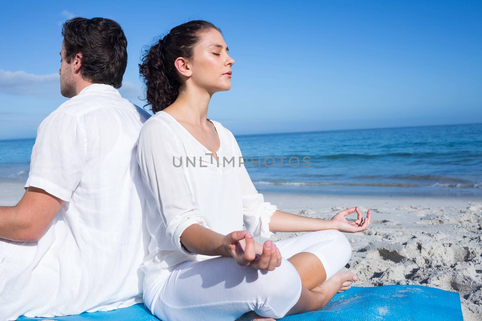 Happy couple doing yoga beside the water at the beach