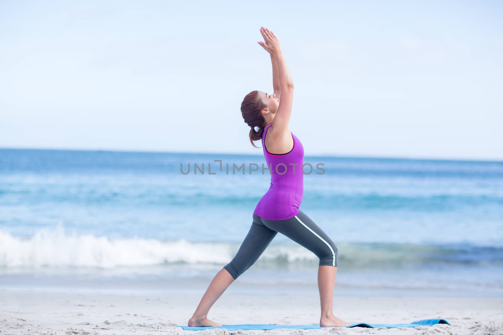 Brunette doing yoga on exercise mat at the beach