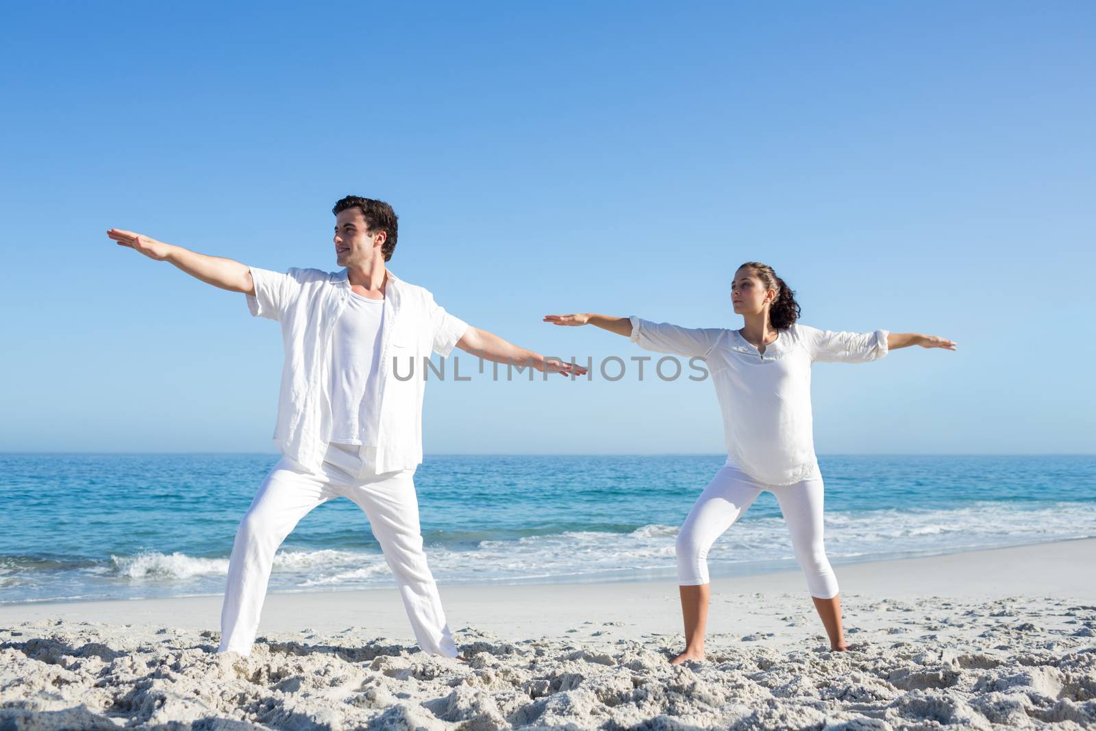 Happy couple doing yoga beside the water at the beach