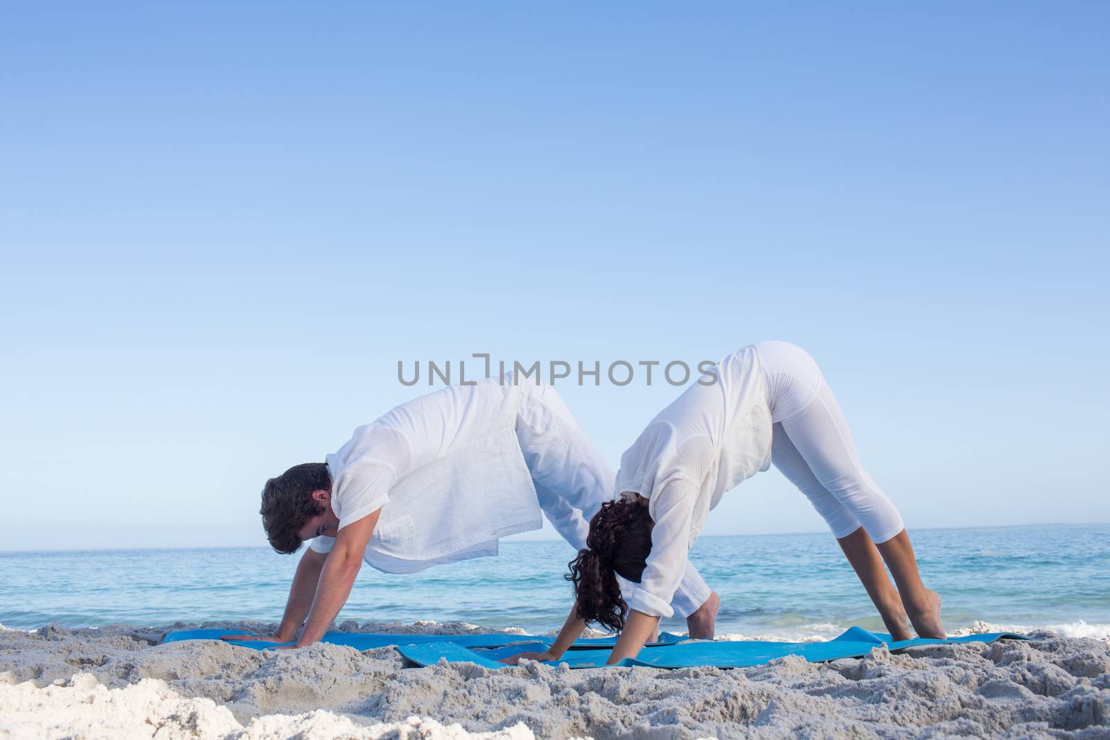 Happy couple doing yoga beside the water by Wavebreakmedia