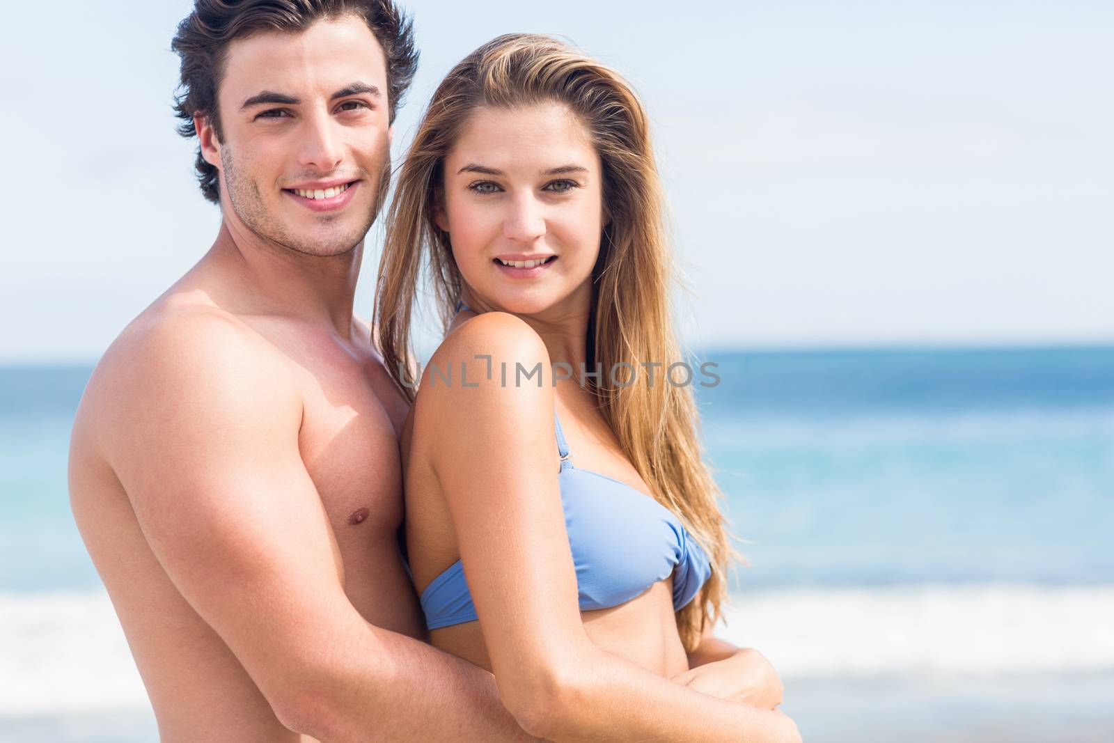 Happy couple in swimsuit looking at camera and embracing at the beach