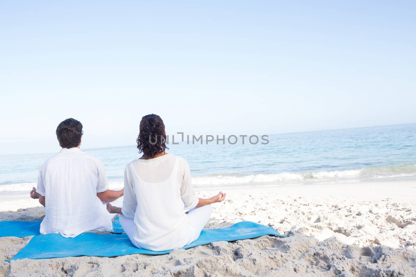 Happy couple doing yoga beside the water by Wavebreakmedia