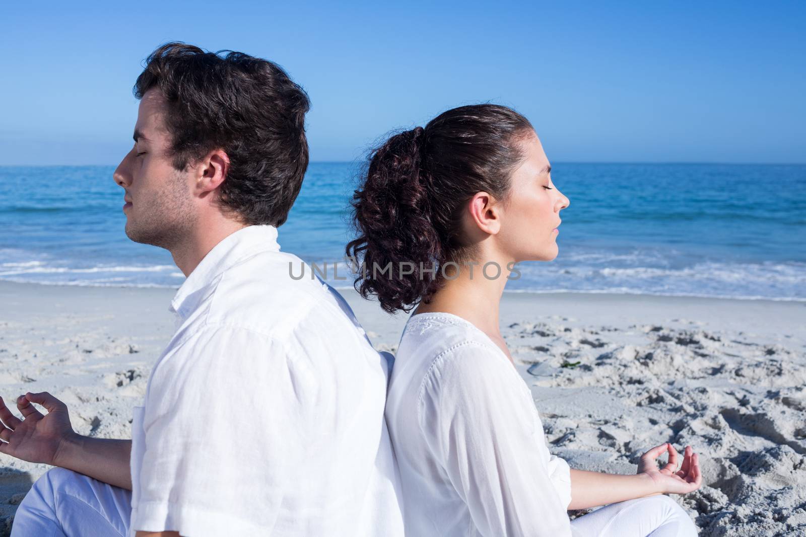 Happy couple doing yoga beside the water at the beach