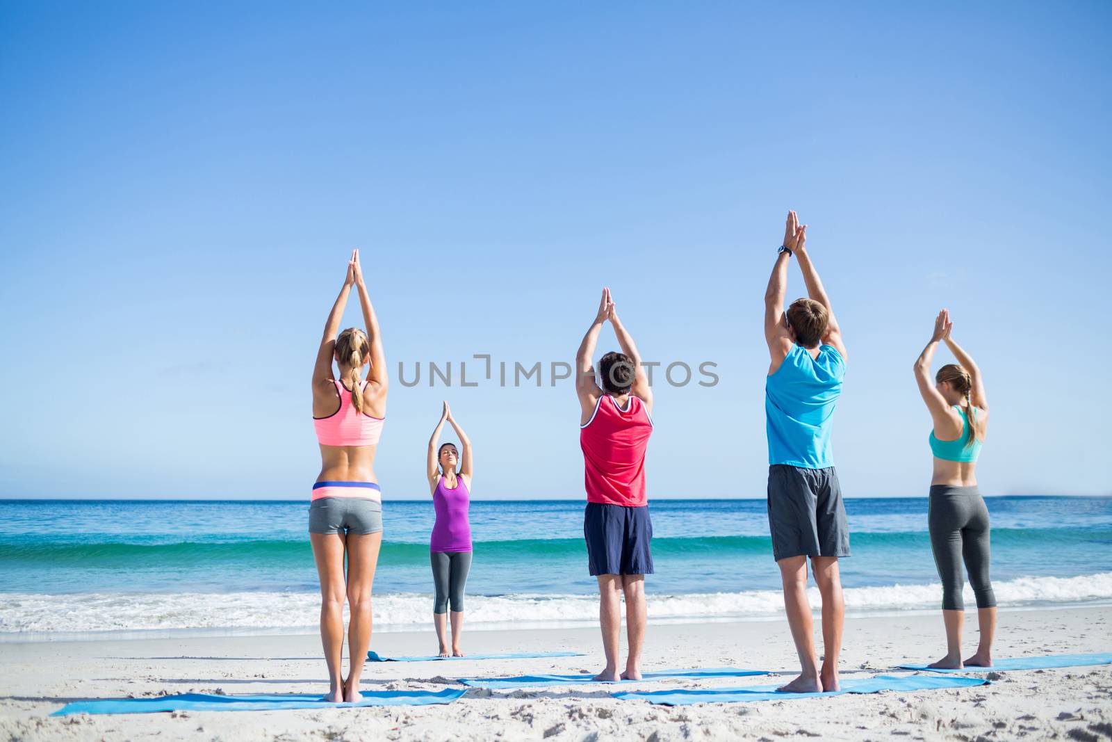 Friends doing yoga together with their teacher at the beach