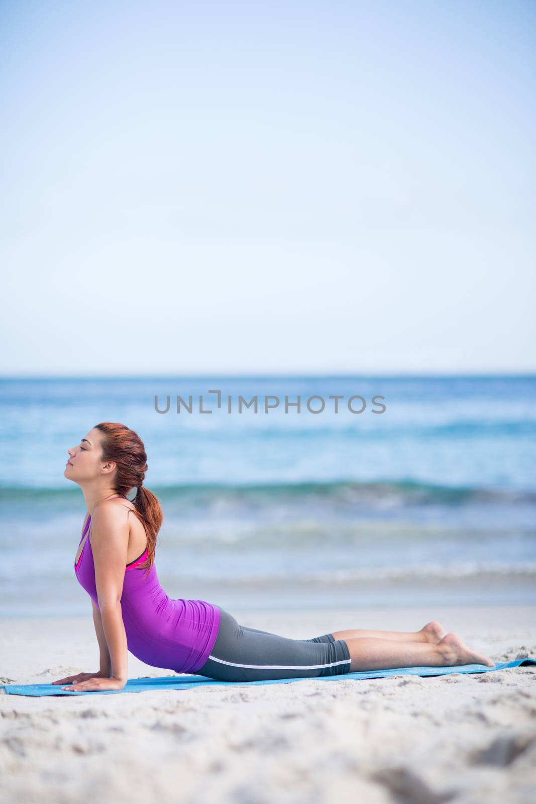 Brunette doing yoga on exercise mat at the beach