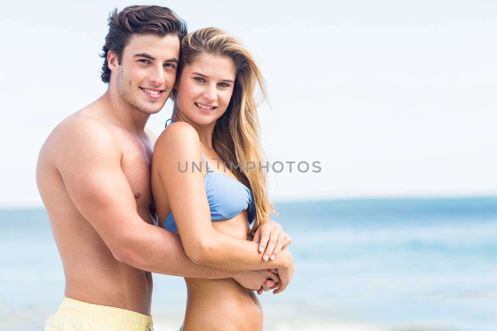 Happy couple in swimsuit looking at camera and embracing by Wavebreakmedia