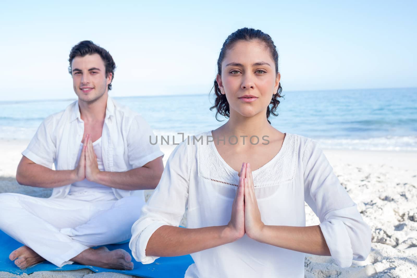 Happy couple doing yoga beside the water at the beach