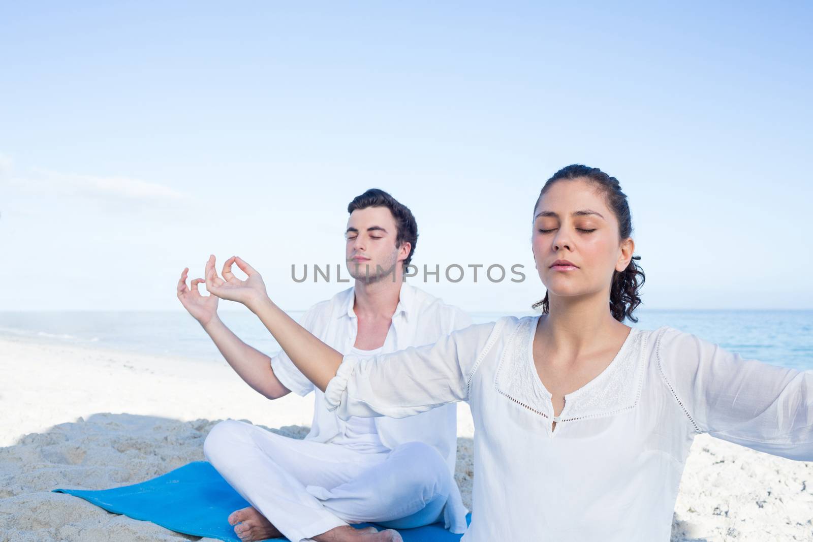 Happy couple doing yoga beside the water at the beach