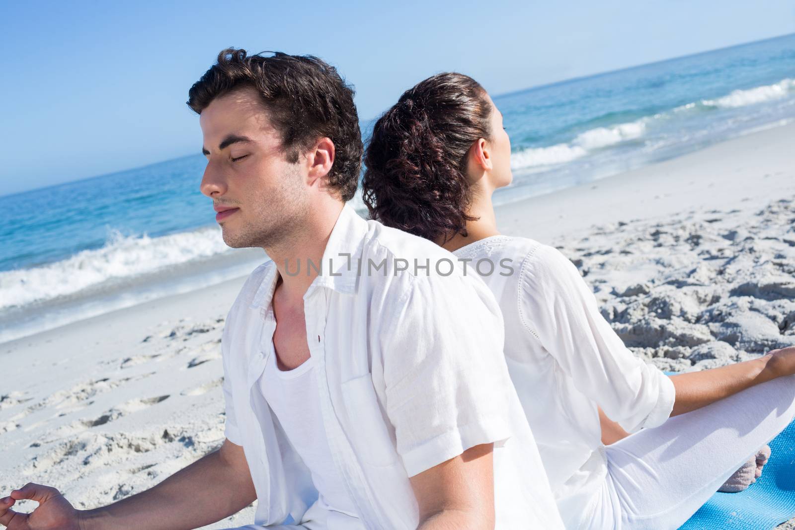 Happy couple doing yoga beside the water at the beach