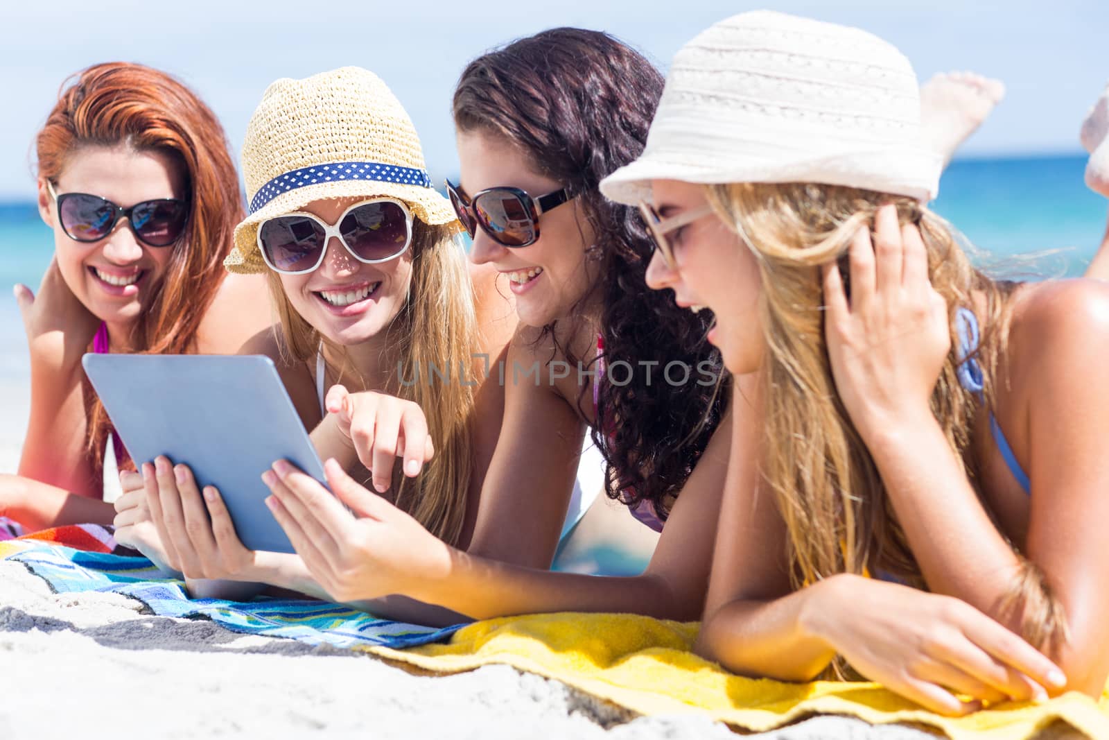 Happy friends wearing sun glasses and using tablet at the beach