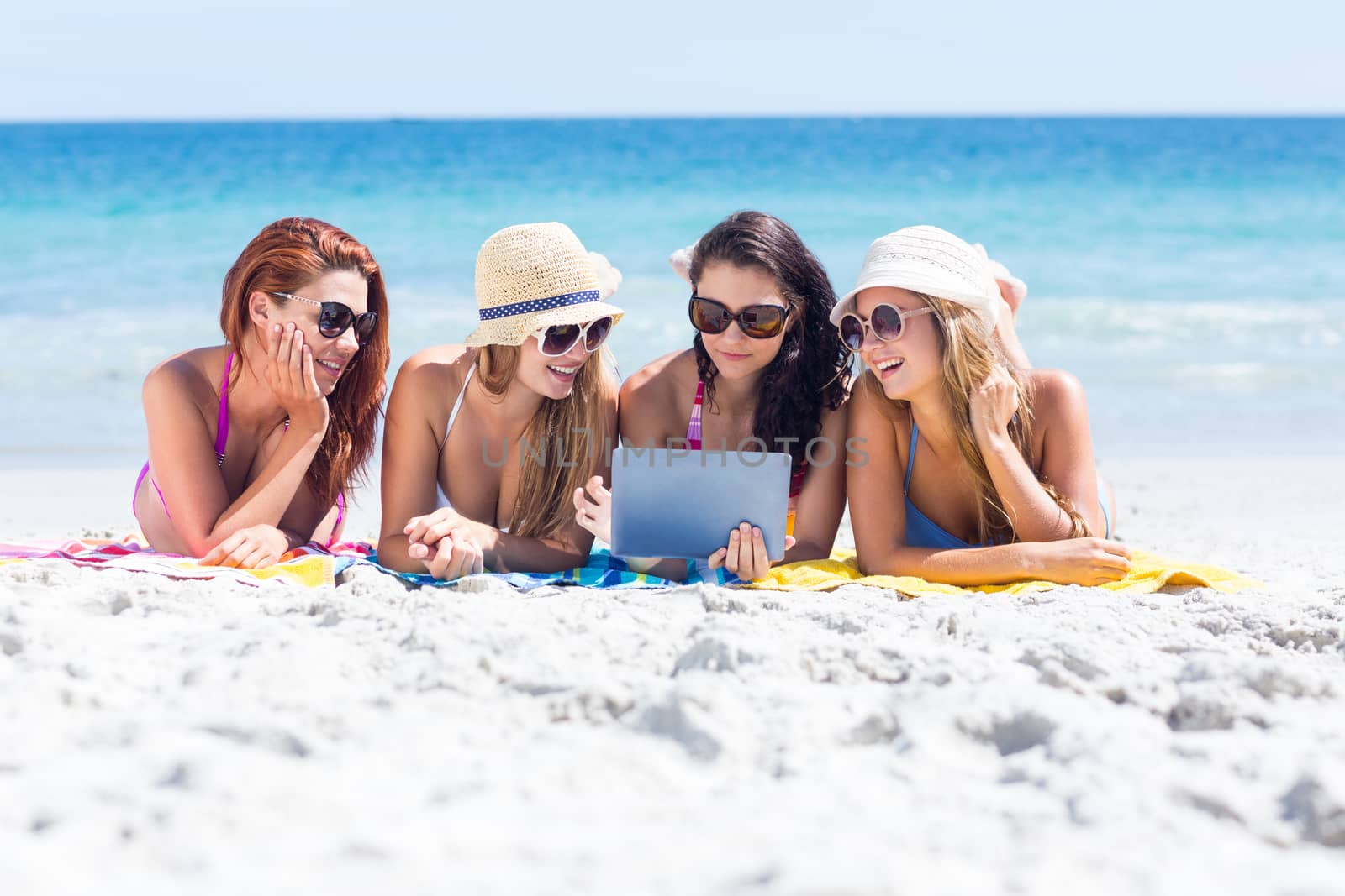 Happy friends wearing sun glasses and using tablet at the beach