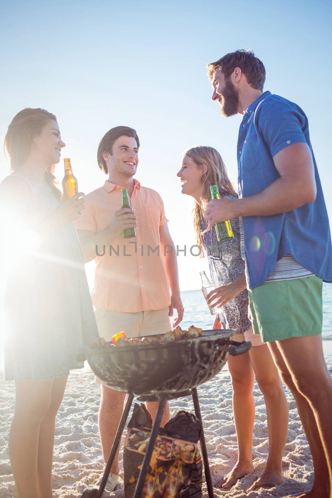 Happy friends doing barbecue and drinking beer at the beach