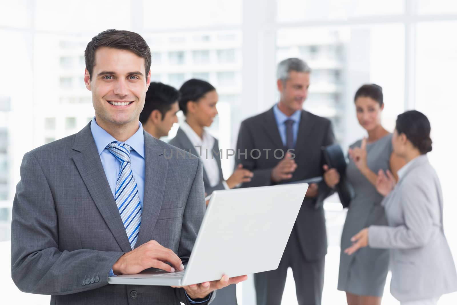 Businessman using laptop with colleagues behind in the office