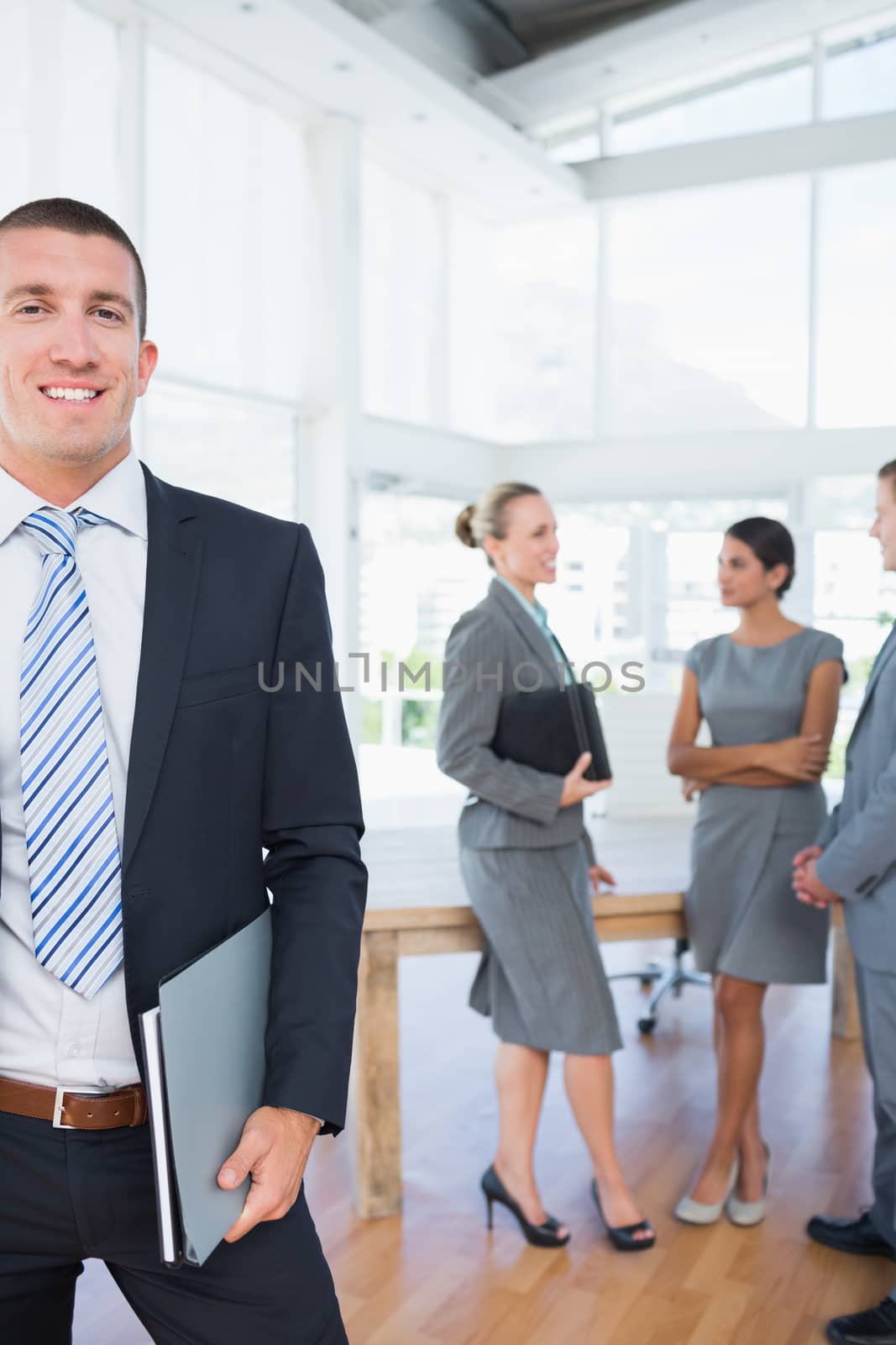 Businessman smiling at camera with colleagues behind him by Wavebreakmedia