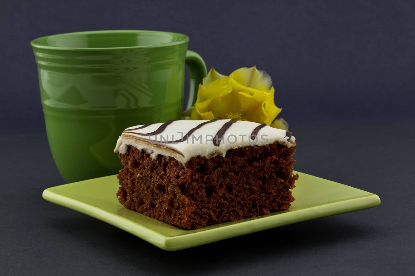 Richly delicious red velvet cake on contemporary green, square plate with classic mug and yellow flower behind.  All on dark background with copy space on right.