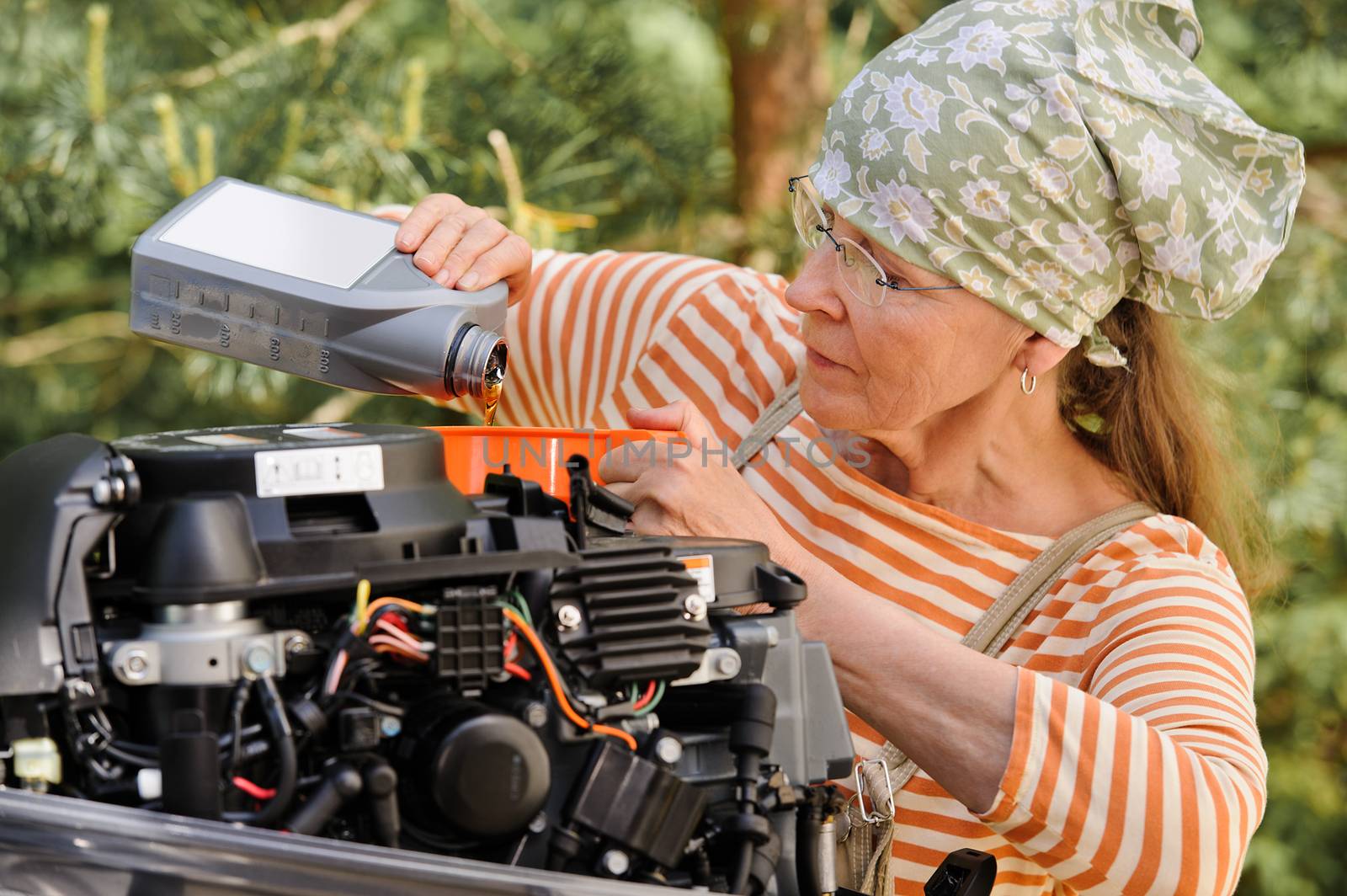 Senior woman pours oil into an outboard engine through a funnel. Breaking down the  stereotypes of women - gender and age