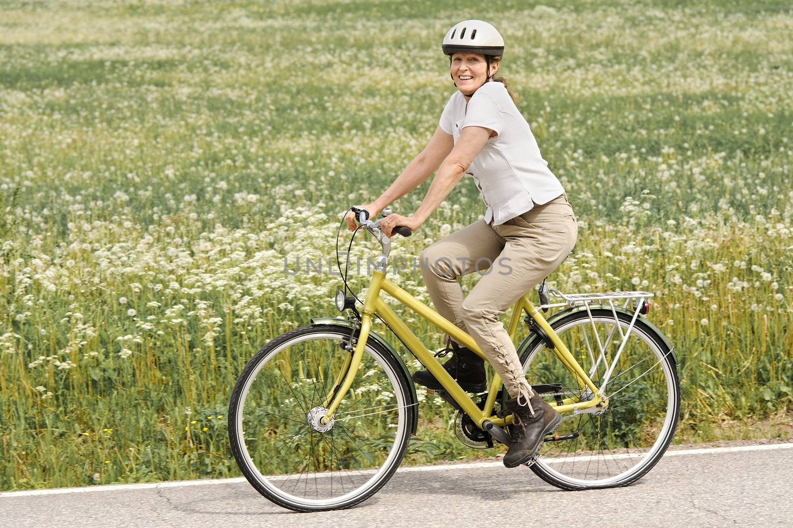 Senior woman vigorously exercising. She's cycling on a country road by the fields.