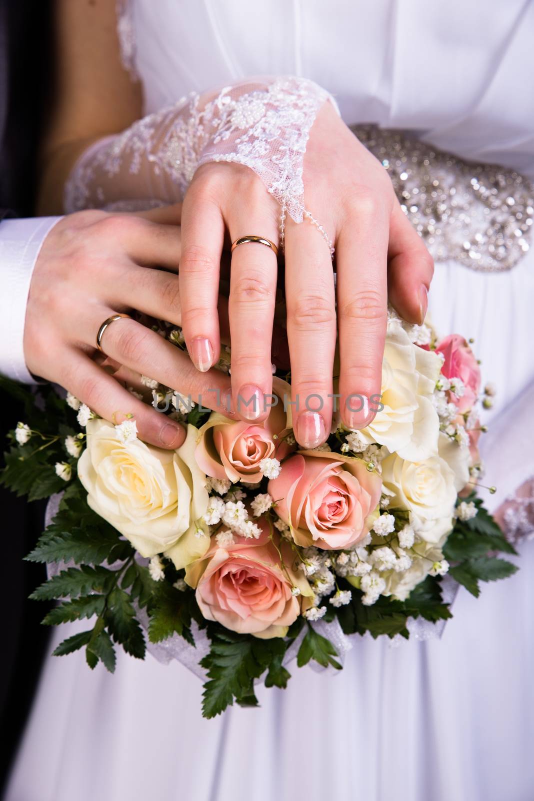 Hands of the newlyweds with wedding bouquet. vertical shot