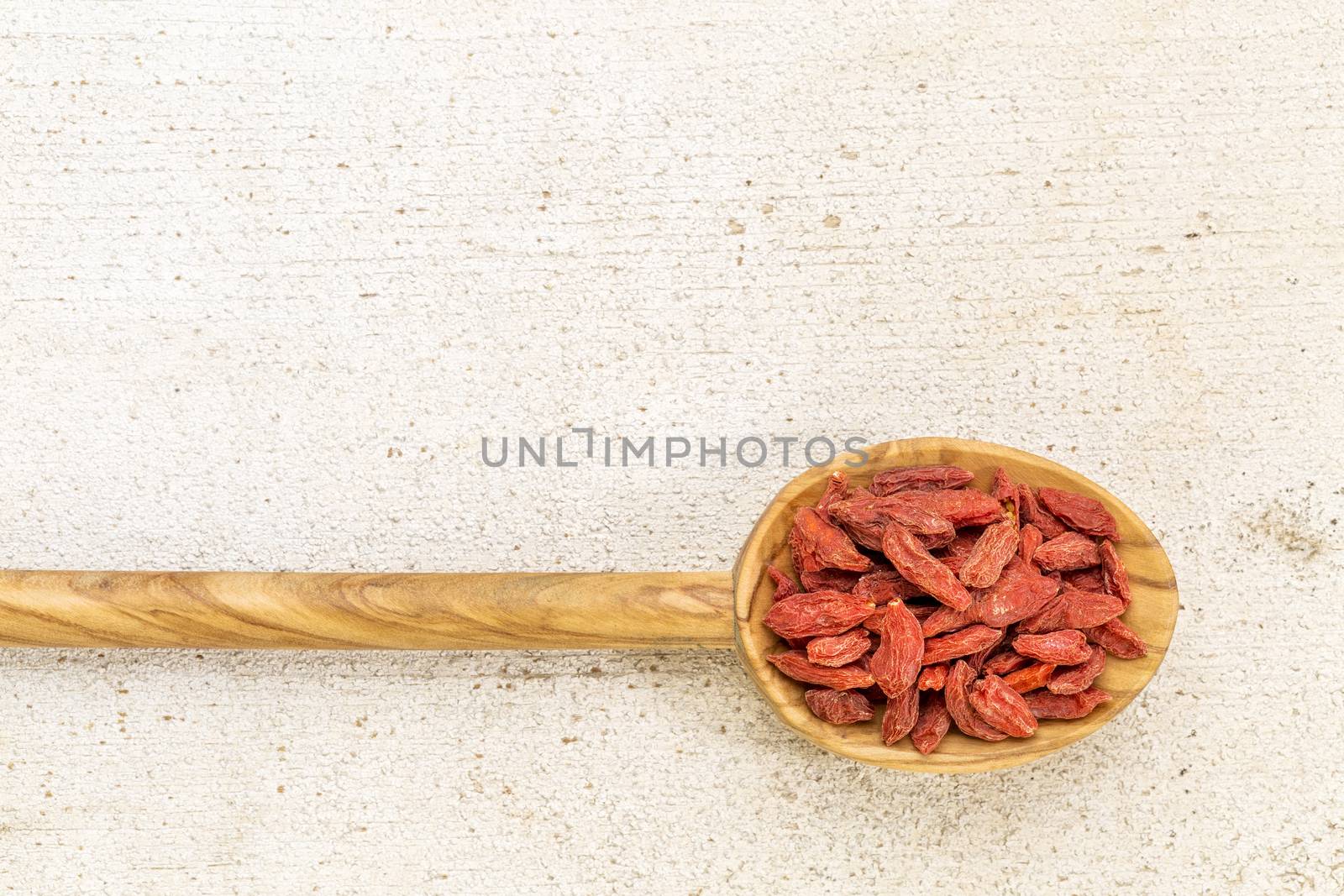 dried goji berries on a wooden spoon against a grunge barn wood with a copy space