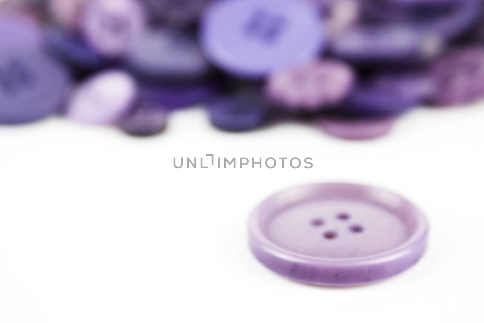 Close up of various purple button scattered on a white surface.