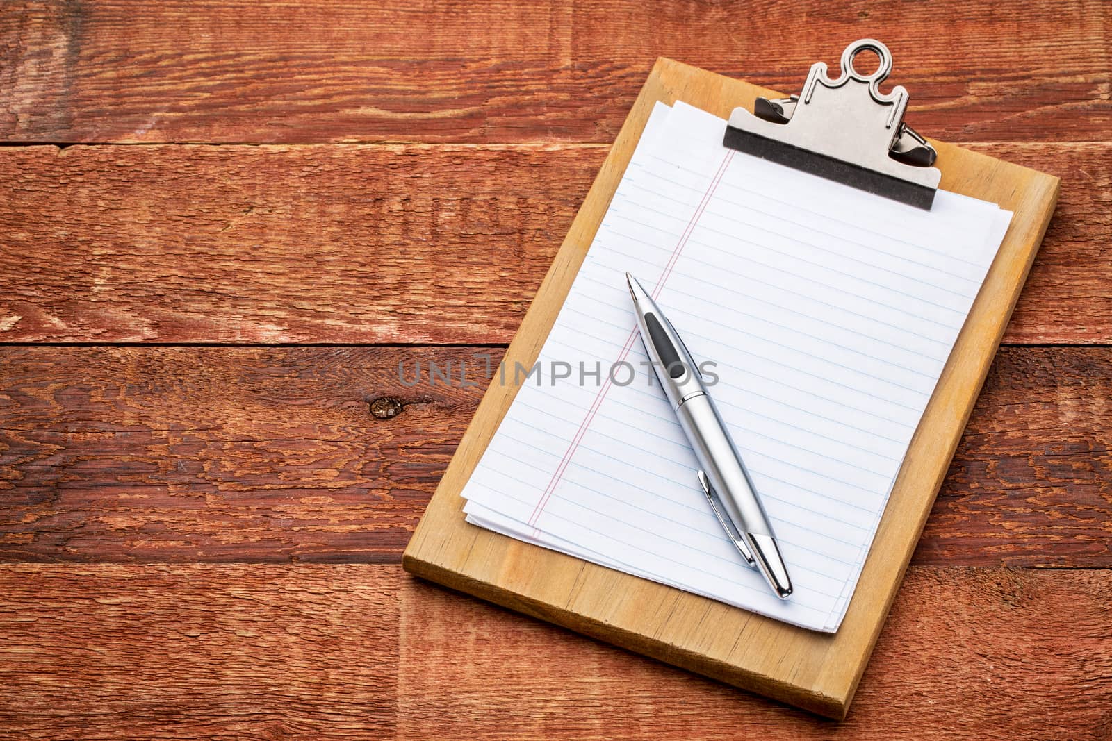 small wooden clipboard with blank paper and pen against rustic barn wood with a copy space