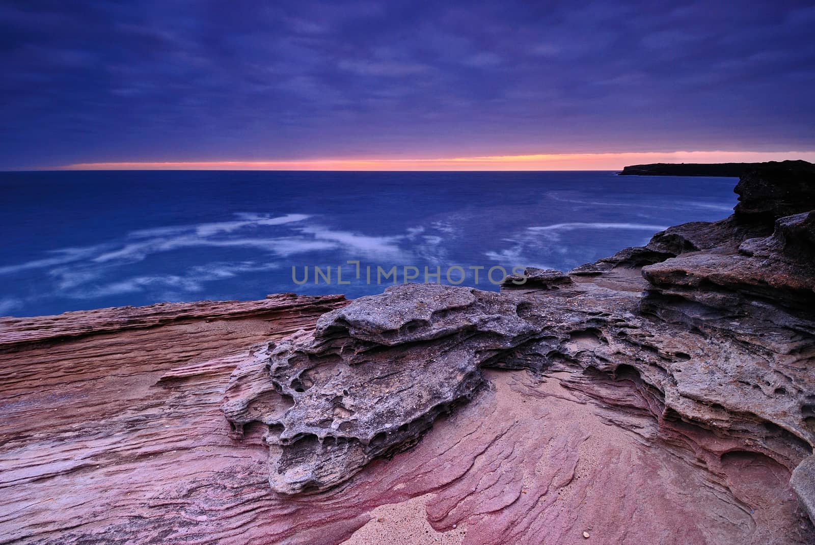 Sunrise seascape with orange rocks and ocean pools and sea shells with cloudy stormy sky and distant cliffs