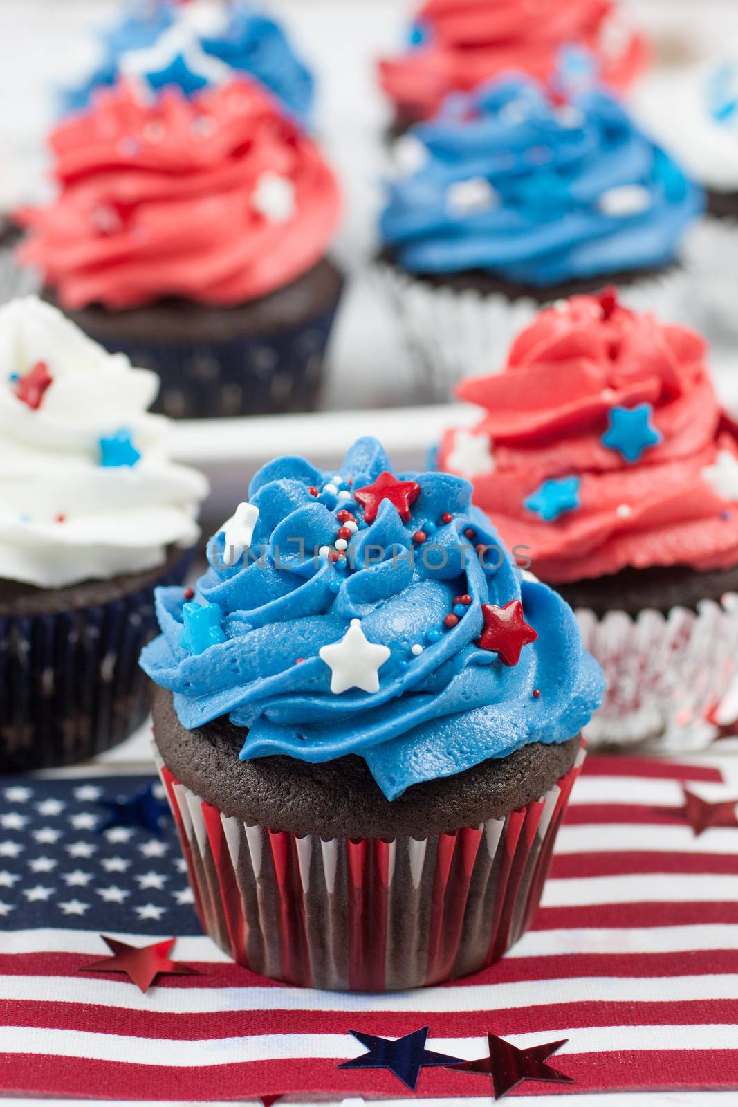 Chocolate cupcakes decorated in red, white, and blue and surrounded by stars and flags in celebration of  Independence Day.