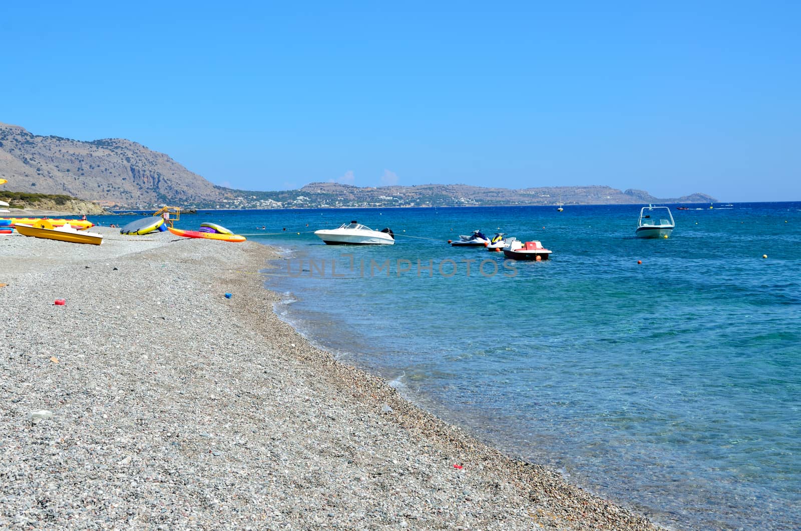 Rhodes Island in Greece. Holiday resort at Kiotari Beach with few boats. Blue sky, turquoise sea, beach covered with small stones. 