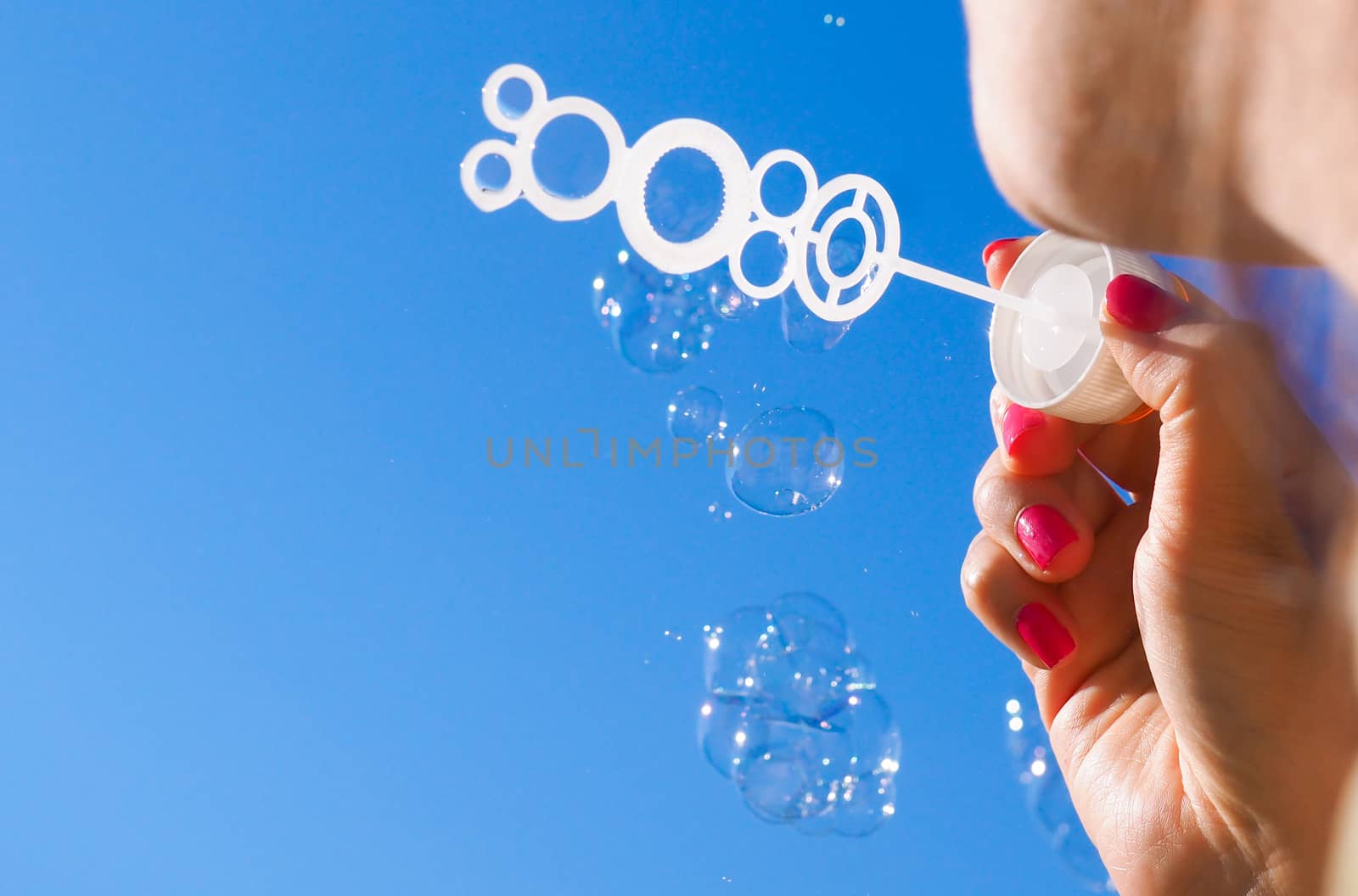 Female person blowing soap bubbles into blue sky by Arvebettum