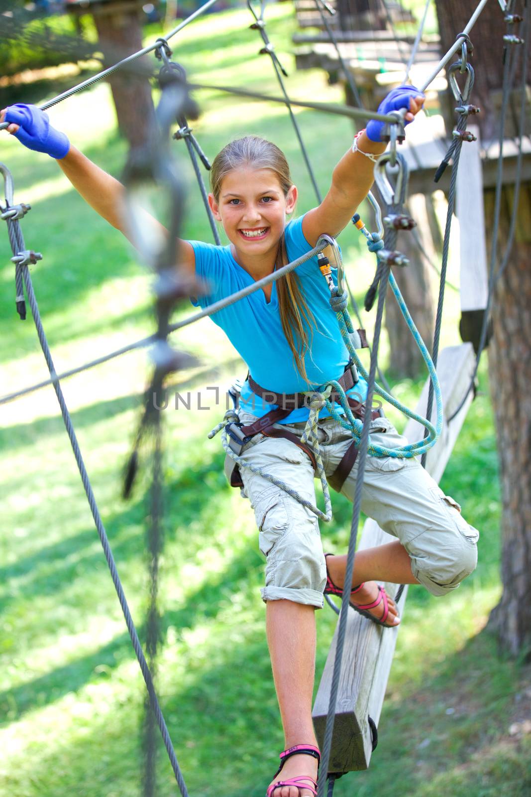 Happy school girl enjoying activity in a climbing adventure park on a summer day