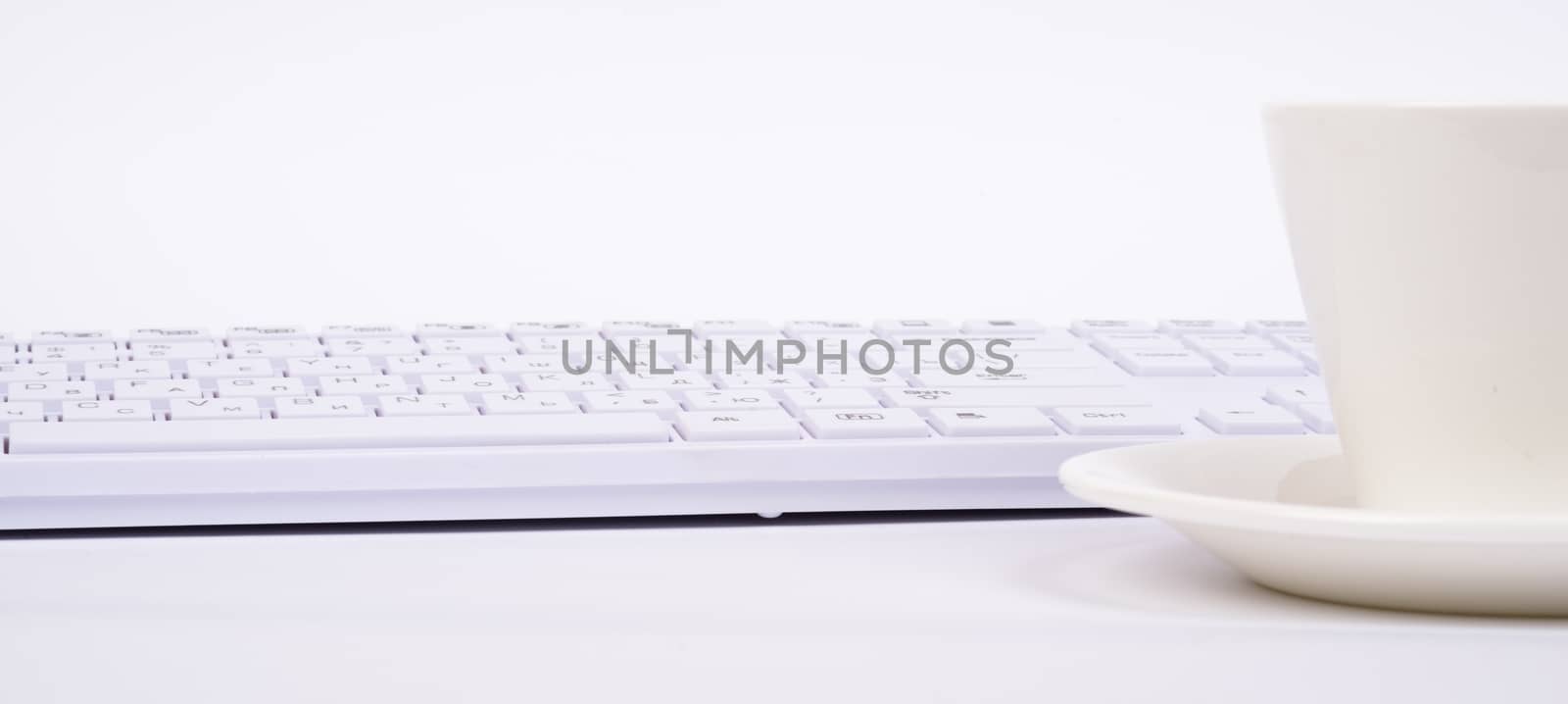Computer keyboard and cup on isolated white background, side view