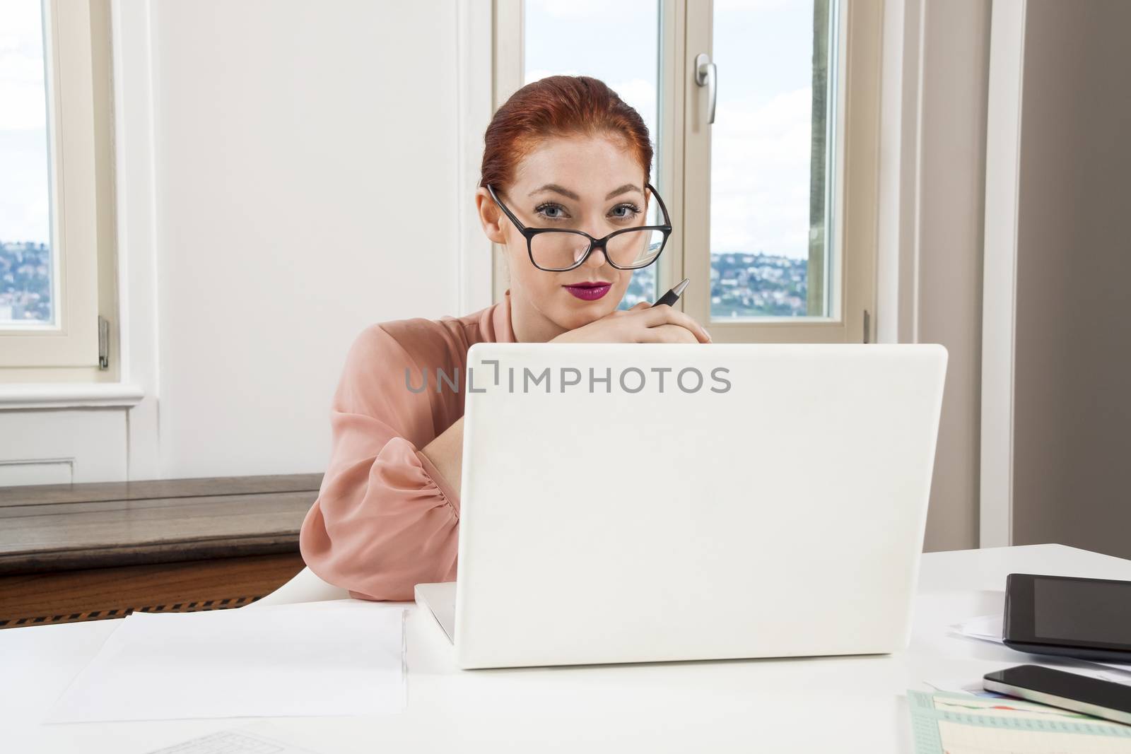 Sitting Young Businesswoman Writing on a Paper While Looking at her Laptop Computer Seriously.