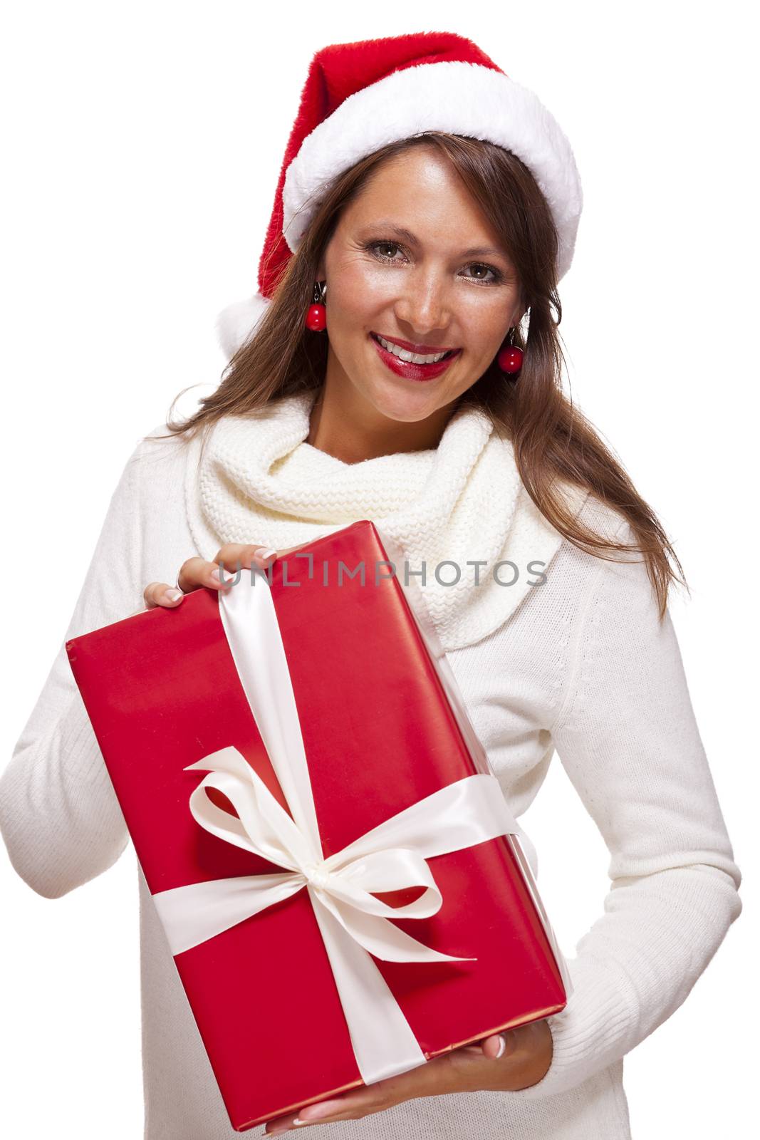 Pretty woman in a festive red Santa hat with a large matching red Christmas gift tied with a ribbon and bow holding it in front of her with a happy smile showing it to the camera, on white