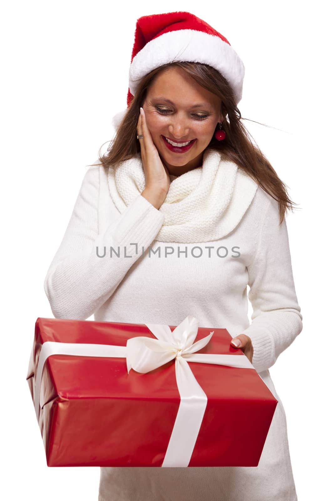 Pretty woman in a festive red Santa hat with a large matching red Christmas gift tied with a ribbon and bow holding it in front of her with a happy smile showing it to the camera, on white