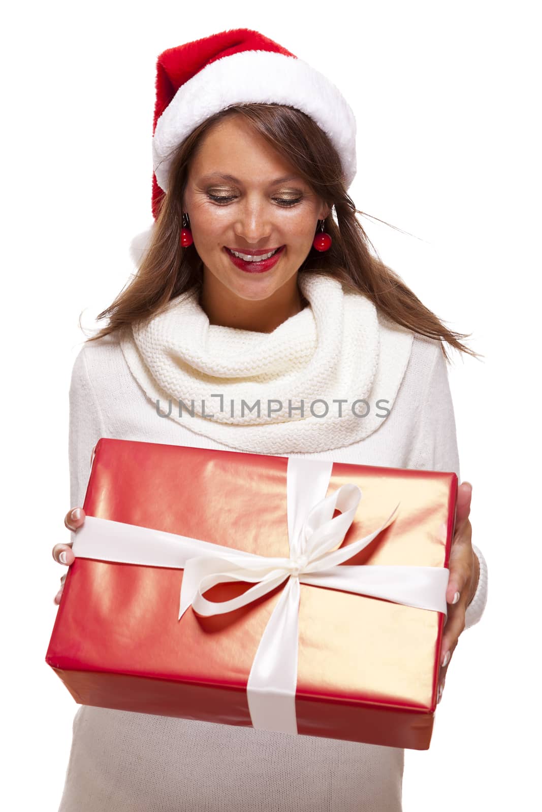 Pretty woman in a festive red Santa hat with a large matching red Christmas gift tied with a ribbon and bow holding it in front of her with a happy smile showing it to the camera, on white